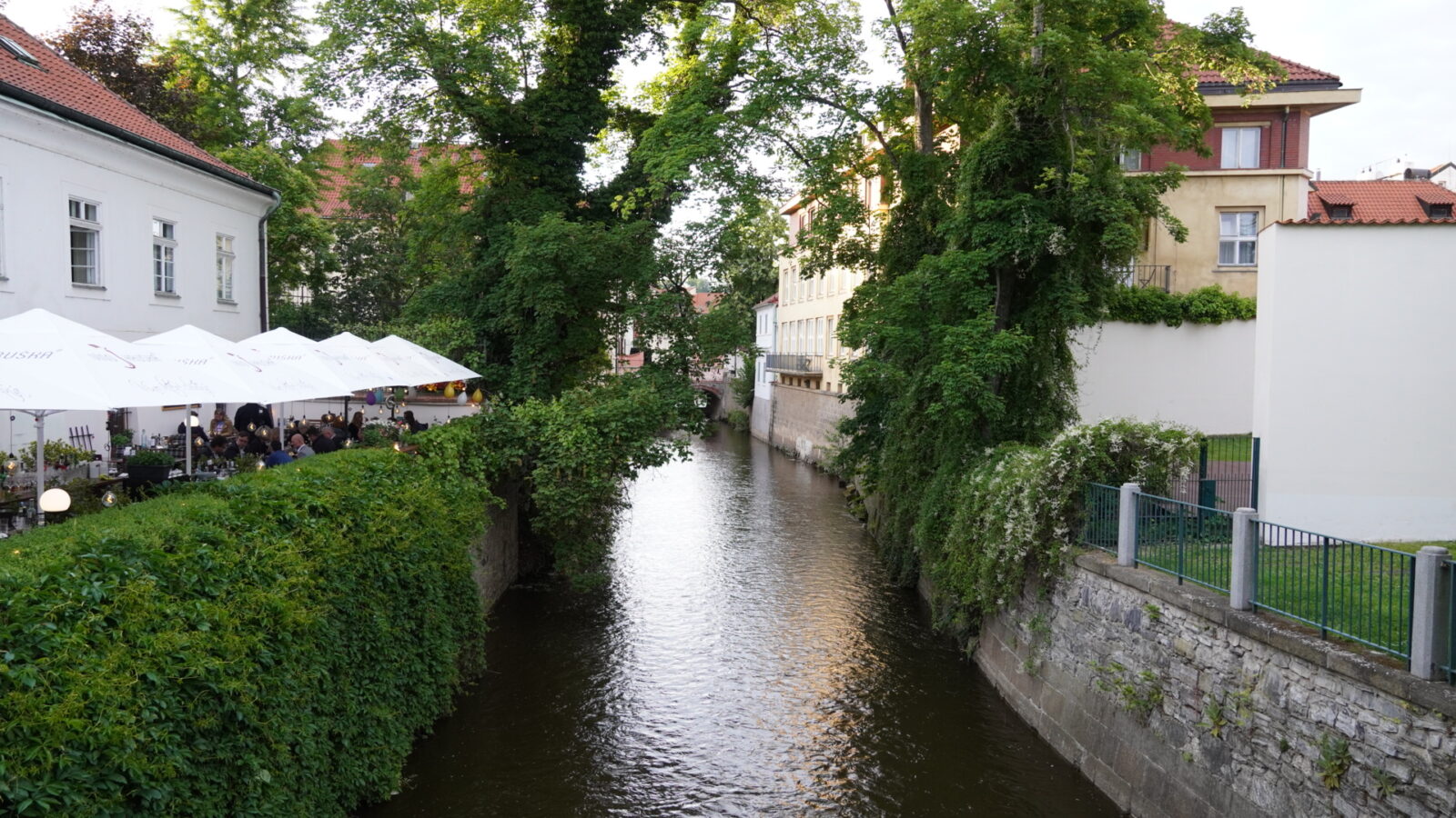プラハの建物と緑のあいだを流れる細い水路とテラス席